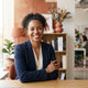 A diverse, smiling professional person in a modern, sunlit office space with warm terracotta and white decor.